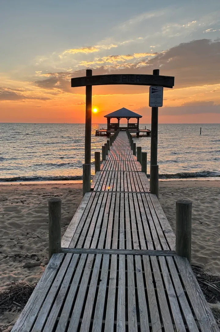 A wooden pier leading toward a covered pavilion over the water at sunset.